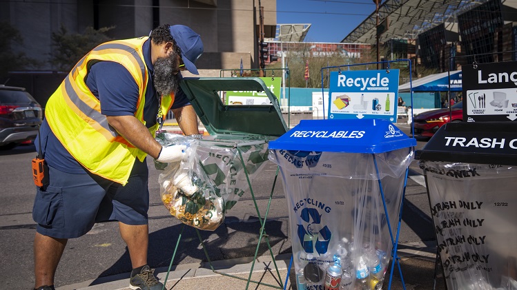 A worker changes a trash bag from a food waste receptacle in downtown Phoenix